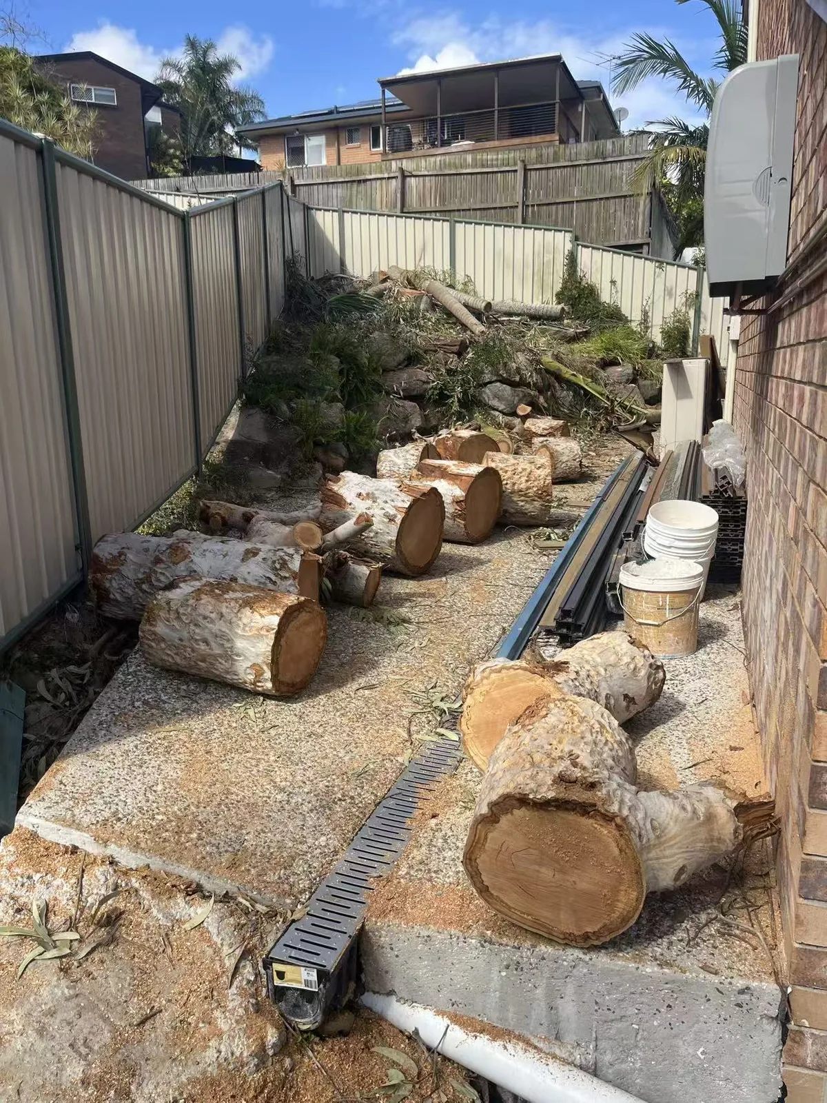 Timber sections stacked along a narrow side access next to a house